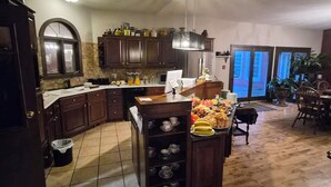 Una cocina con armarios de madera, una isla central con tazas de té y un comedor con sillas.