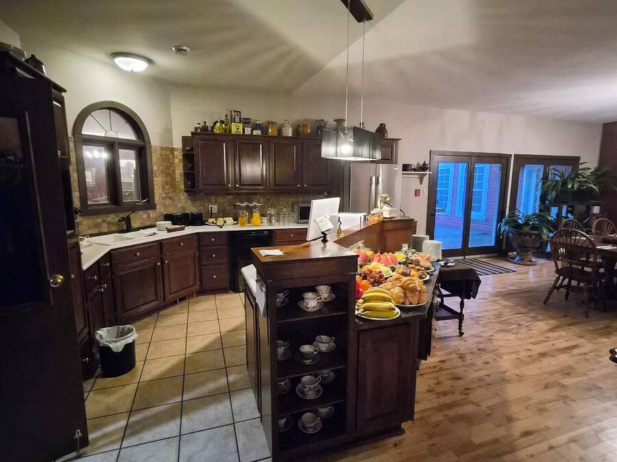A kitchen with wooden cabinets, a central island with tea cups, and a dining area with chairs.