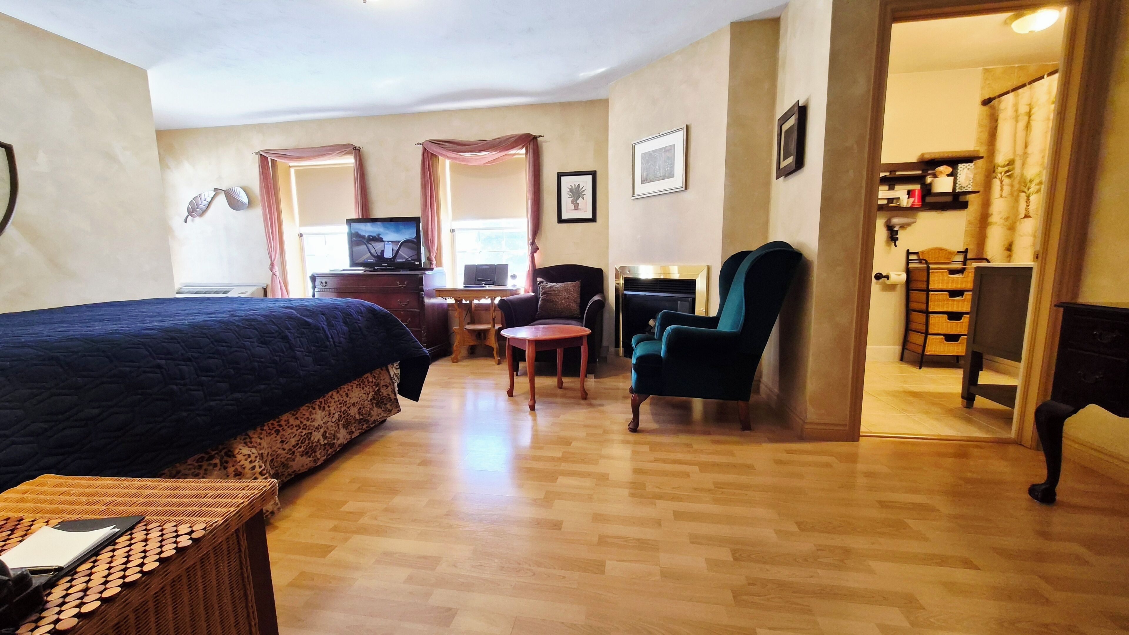 Quarto de hotel com uma cama, uma escrivaninha com computador, uma cadeira, uma mesinha e uma televisão.