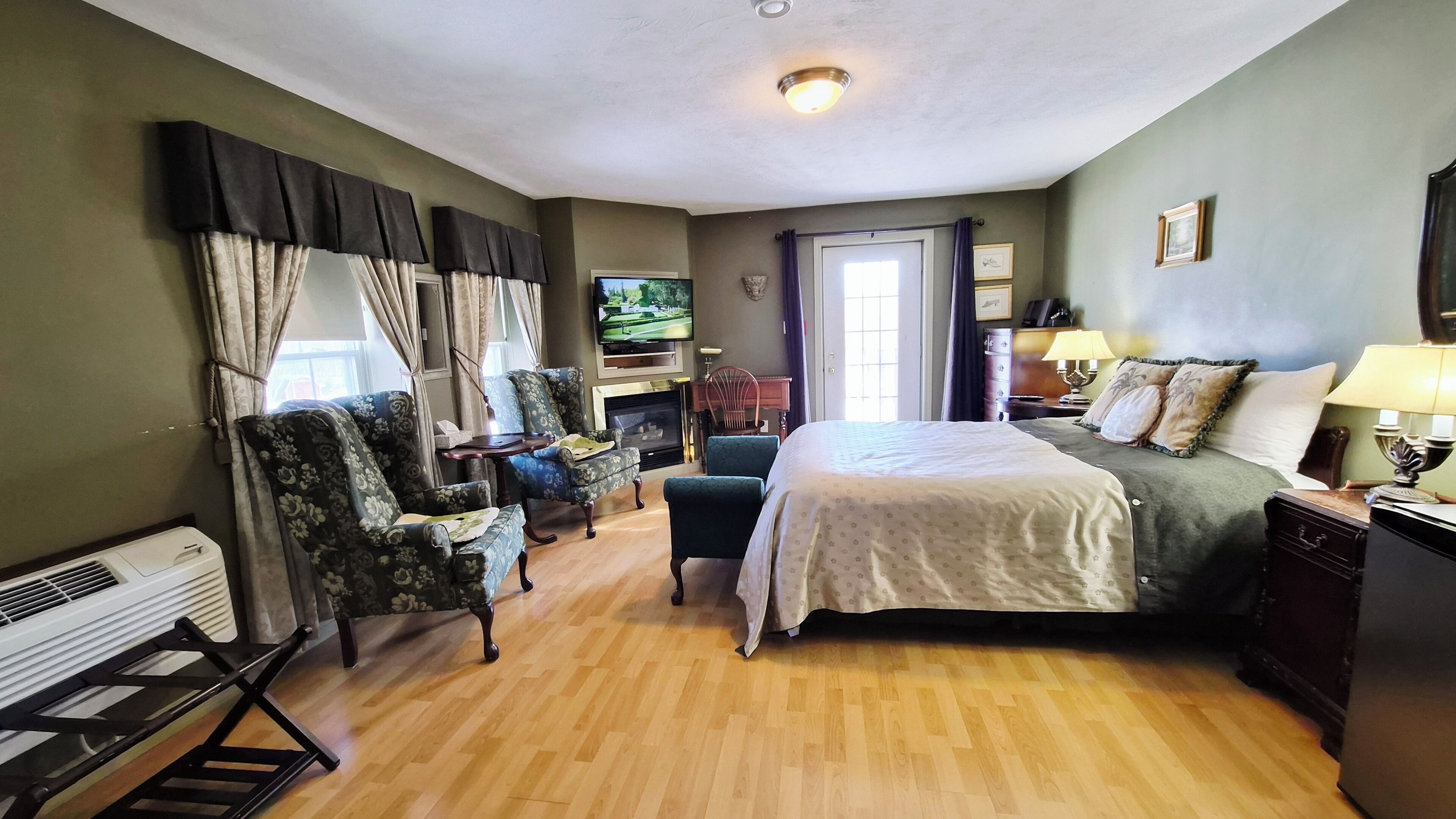 A hotel room with a bed, two armchairs, a small table, a fireplace, and a television.