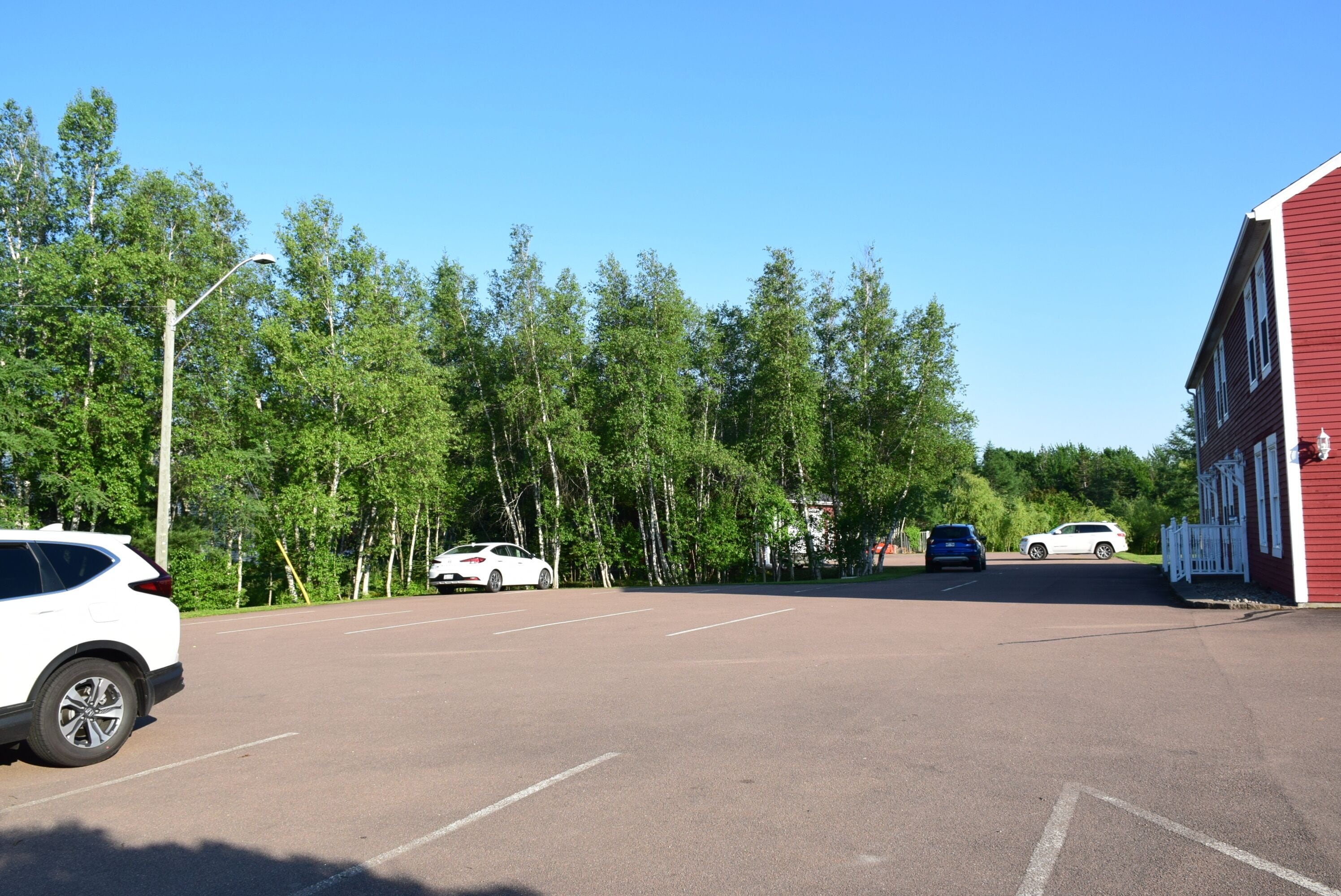 A parking lot with several cars, a red building with white trim, and a row of trees in the background.