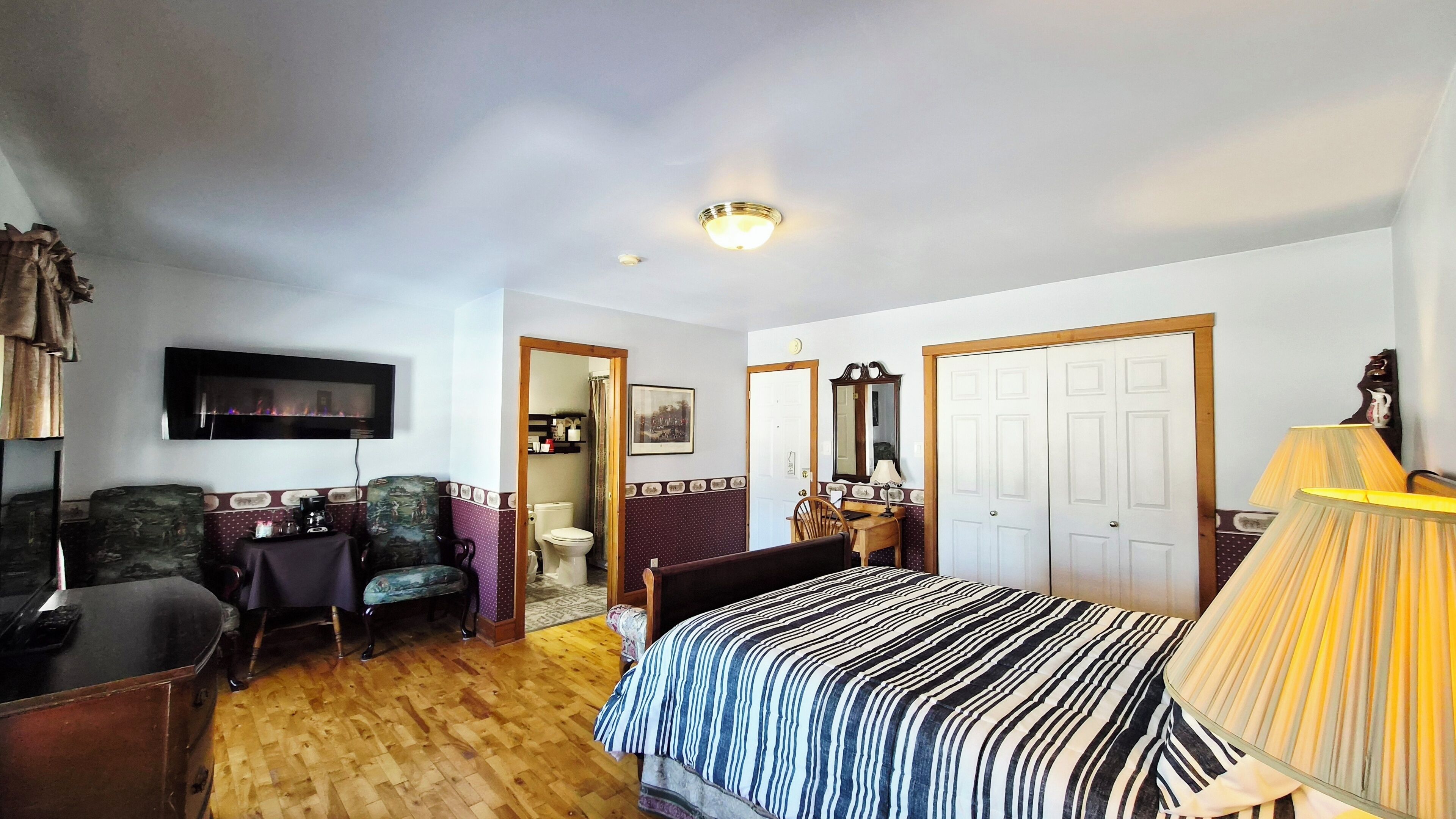 A hotel room with a bed, a desk, a chair, a television, a mirror, and a wardrobe.