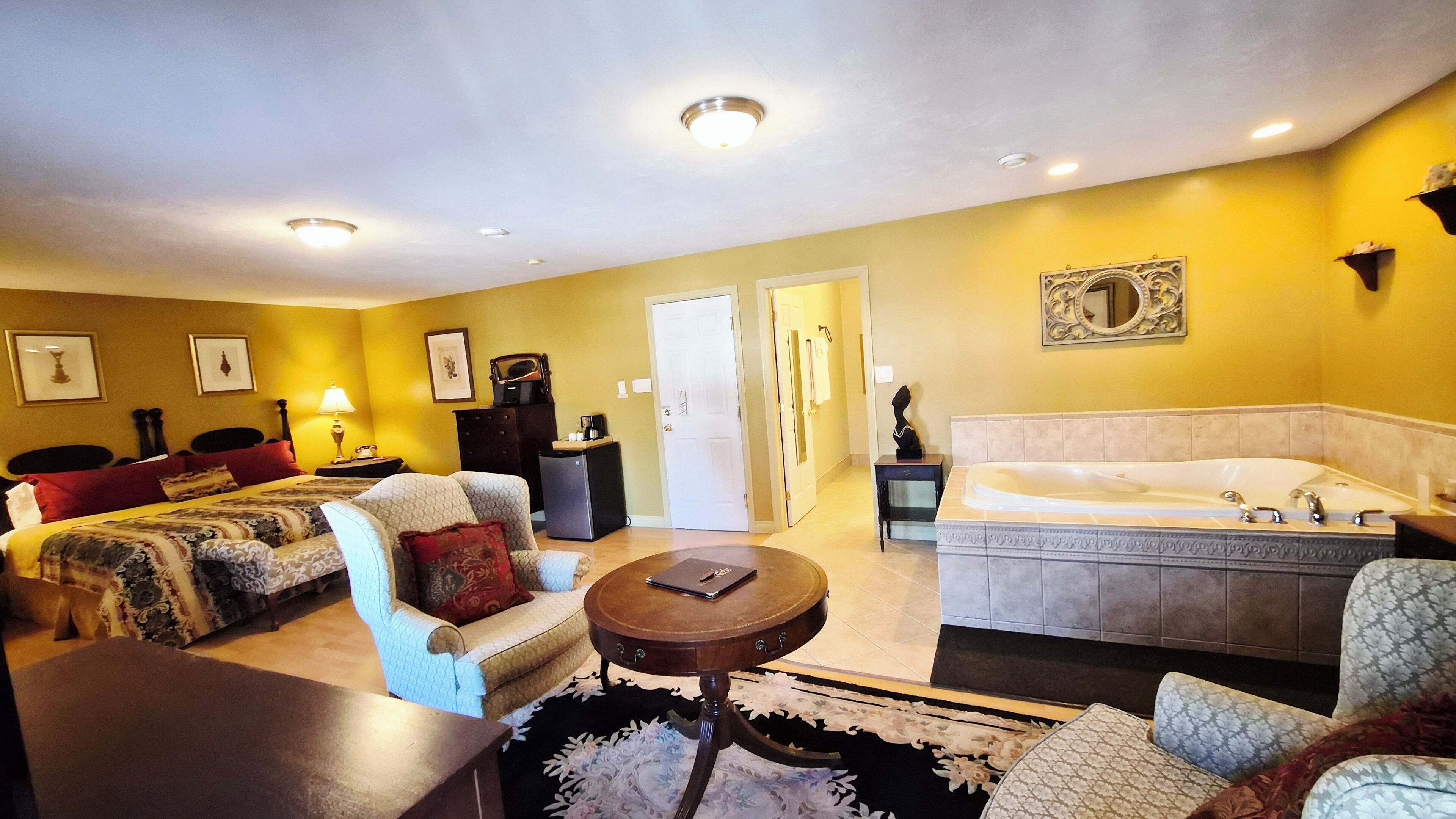 A hotel room with a bed, a sofa, a small table, a bathtub, and a door leading to another room.