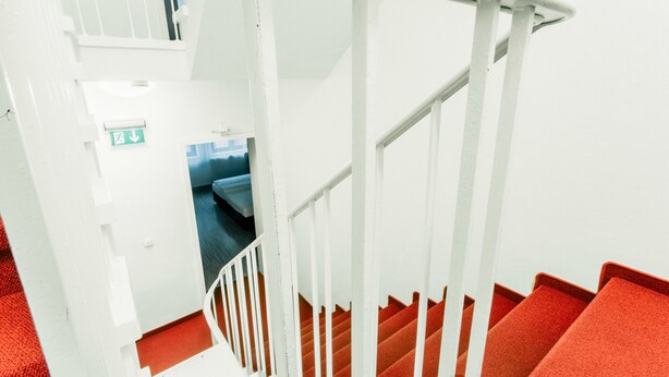 A staircase with white railings and red carpeted steps. - Fair Hotel Mönchengladbach (Moenchengladbach)