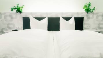 Ein Hotelzimmer mit einem großen Bett, zwei Nachttischen, einer Ablage und zwei Pflanzen an der Wand.