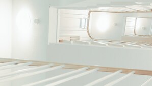Una habitación minimalista con un espejo grande, piso de madera y estructura de cama blanca.