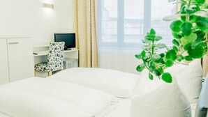 Una habitación de hotel con cama, escritorio, computadora, silla y ventana con cortinas.