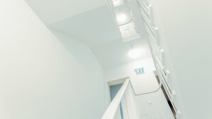 Un corredor interior luminoso y blanco con una escalera y una señal de salida.