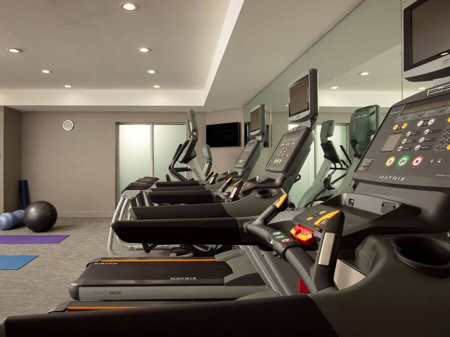 Un gimnasio con cintas de correr, pelotas de ejercicios y un reloj en la pared.
