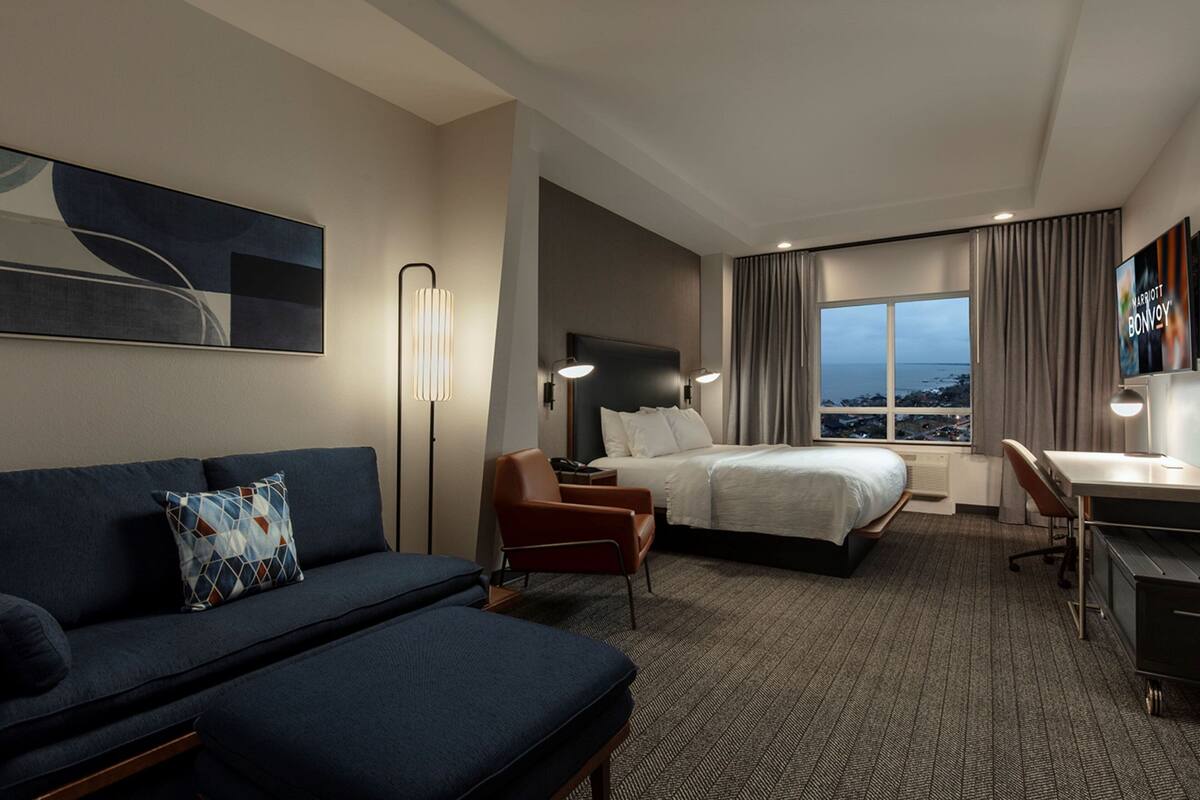 Ein Hotelzimmer mit Bett, Schreibtisch, Sessel, Sofa, Lampe und Meerblick.