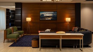 A modern living room with a flat-screen TV, two floor lamps, a sofa, a coffee table, and a small rug. - Courtyard by Marriott Houston Kemah (Kemah)