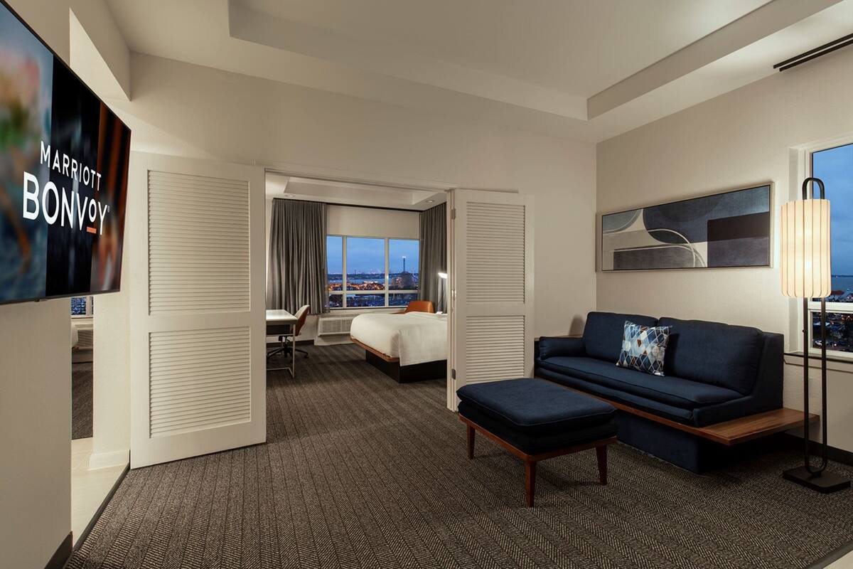 Ein Hotelzimmer mit Bett, Schreibtisch, Sofa, Fernseher und Blick auf die Stadt.