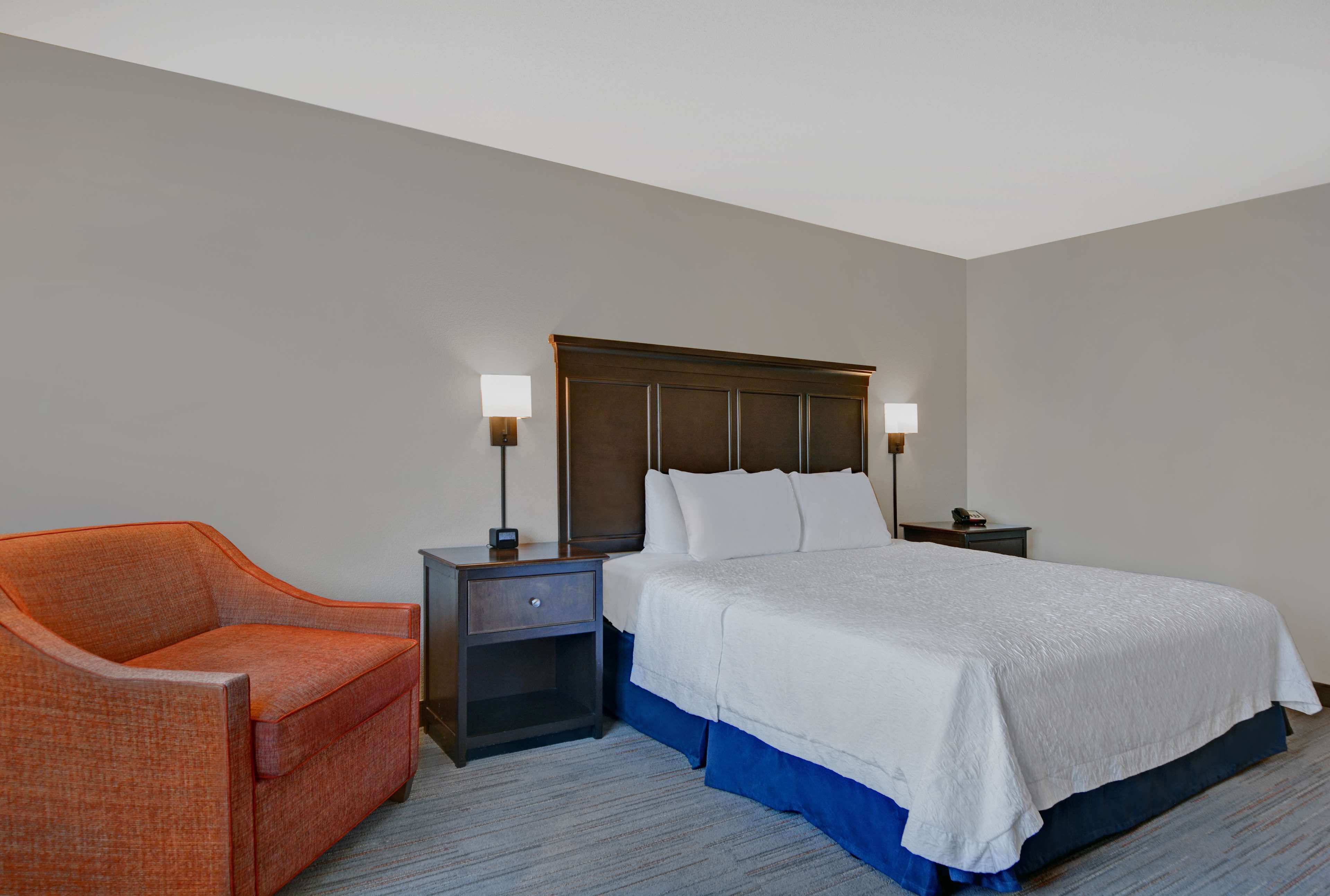 A hotel room with a bed, nightstands, a chair, and a lamp.