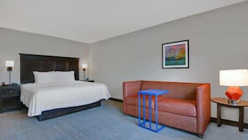 A hotel room with a bed, a sofa, a small table, and a nightstand.