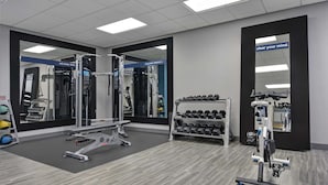 Uma academia com equipamento de exercícios, um espelho e um suporte com halteres.