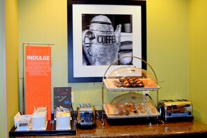 A breakfast buffet with various food items, a coffee pot, and a sign with motivational phrases.