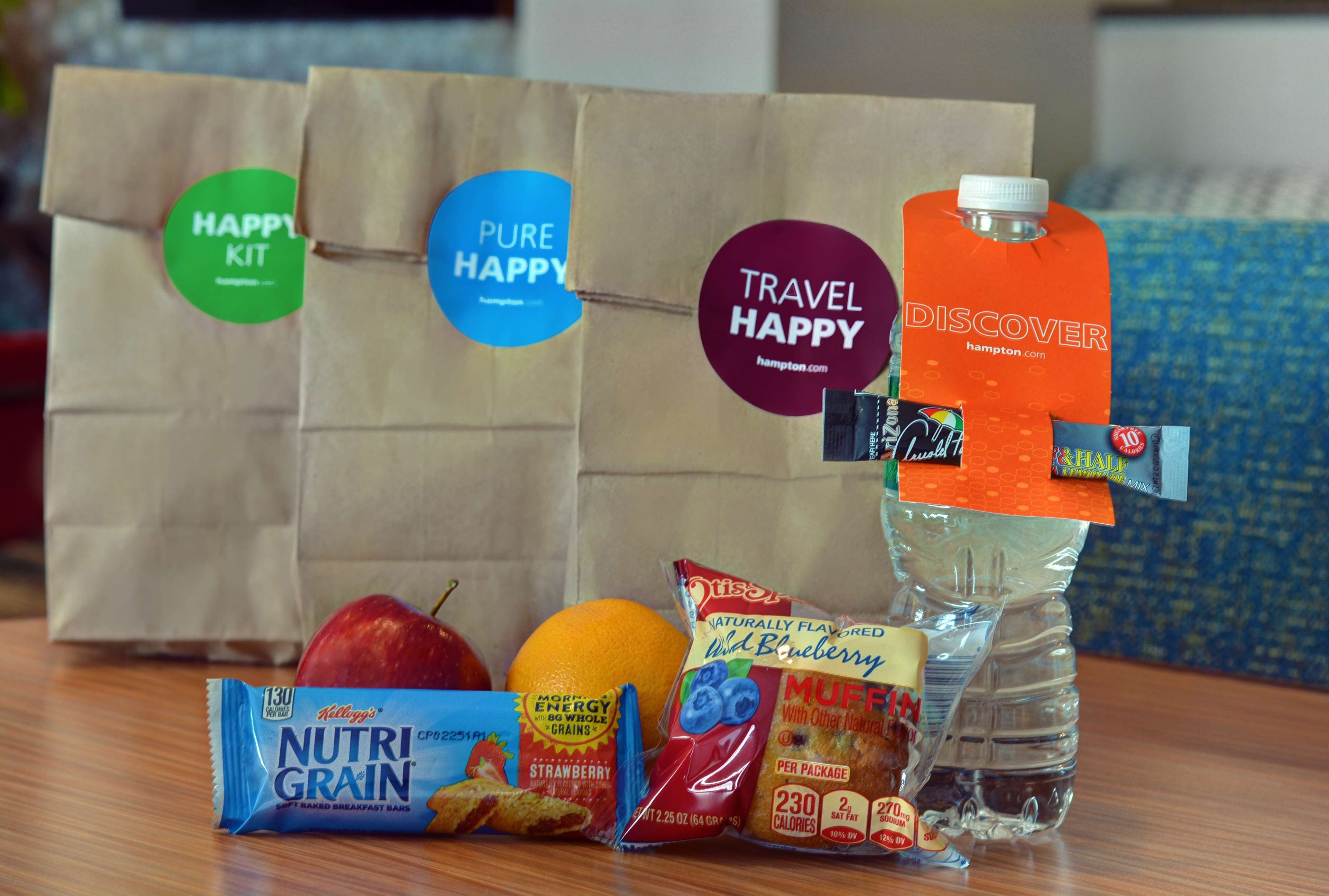 A table with a water bottle, a carton of orange juice, a bag of cereal, a packet of muffins, and a bag of apples.
