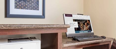 A hotel workspace with a desktop computer, HP LaserJet Pro M404n printer, and a framed geometric artwork on the wall.