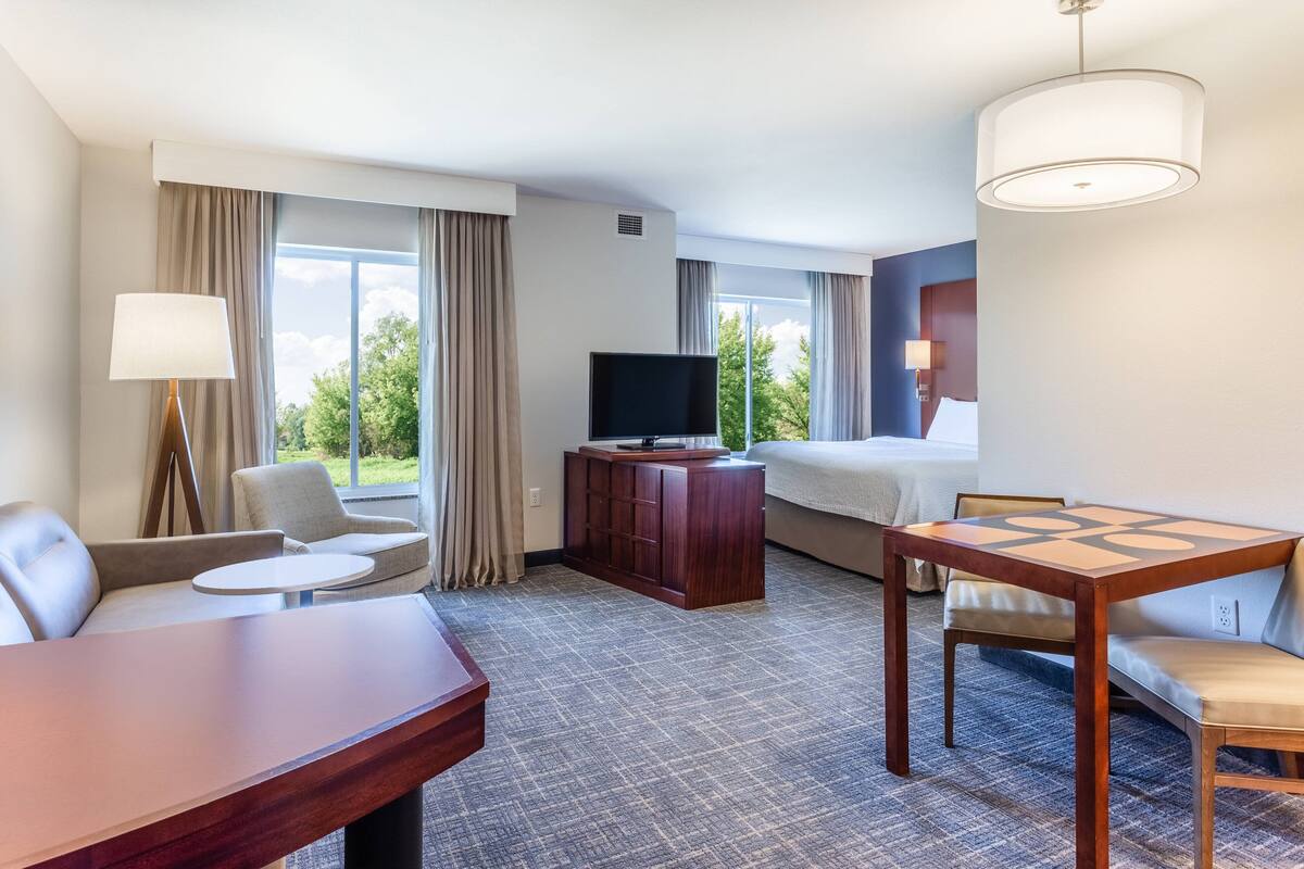 A hotel room with a sofa, a small table, a TV, a cabinet, and a large window with curtains.