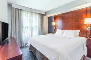 Habitación de hotel con una cama grande, un televisor de pantalla plana, un escritorio de madera y una ventana con cortinas.