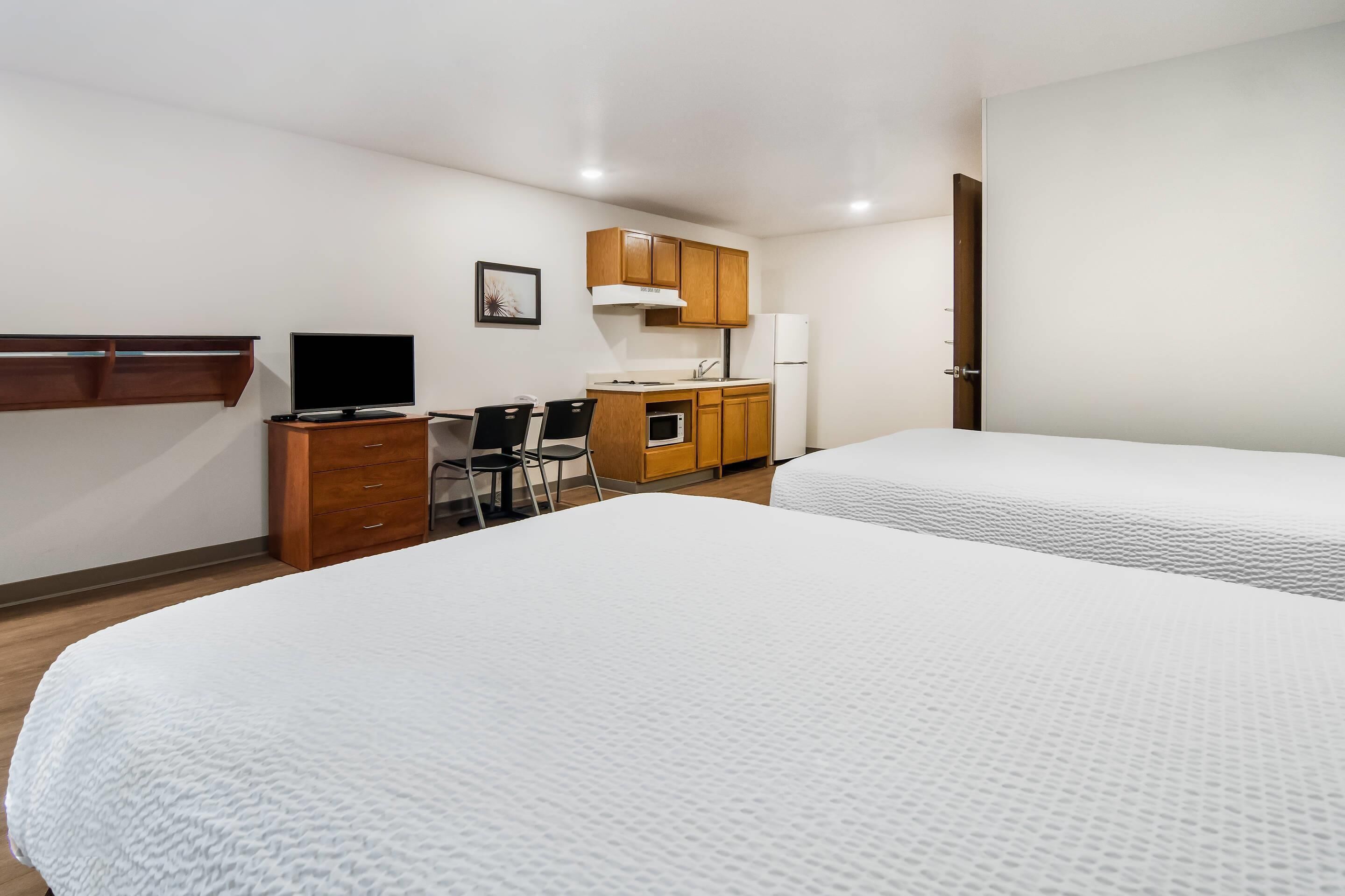 A bedroom with two beds, a desk with a computer, a microwave, and a small kitchenette.