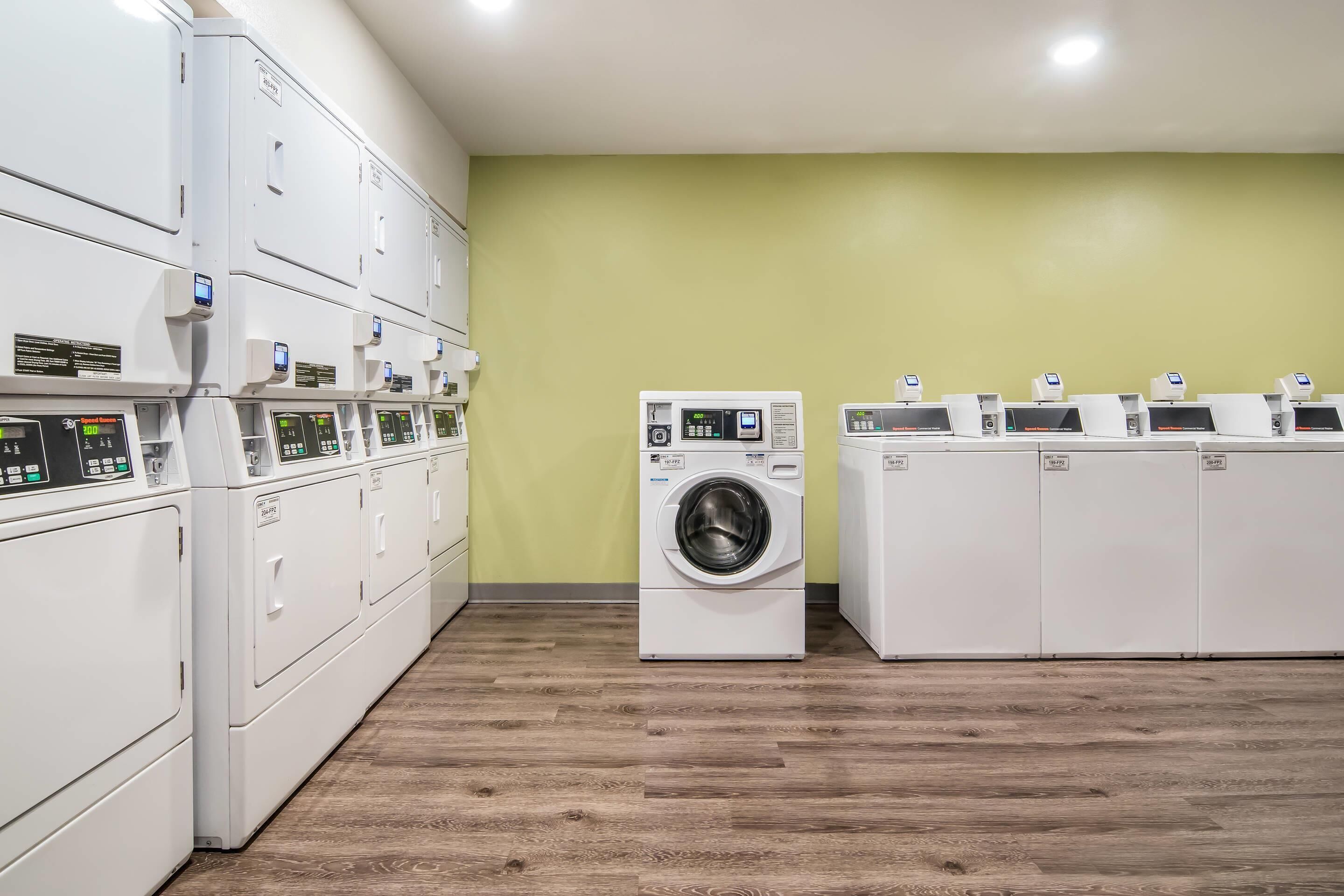 A laundry facility with multiple washing machines and dryers, wooden flooring, and a green wall.