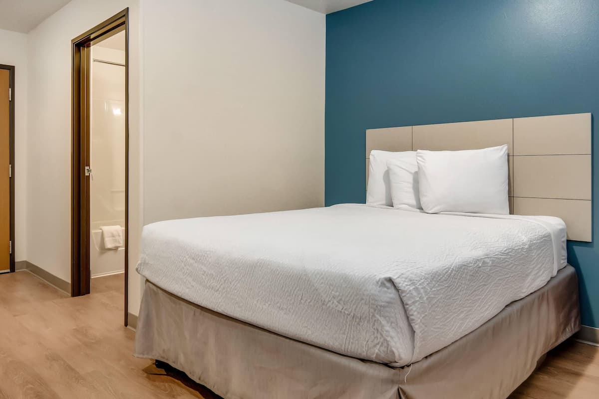 A hotel room with a bed, a door, and a blue wall.