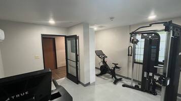Un gimnasio con equipo de ejercicio, una cinta de correr y una puerta que da a otra habitación.