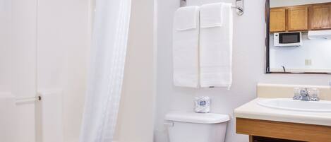 Et badeværelse med toilet, håndvask, bruseforhæng og et håndklædestativ.