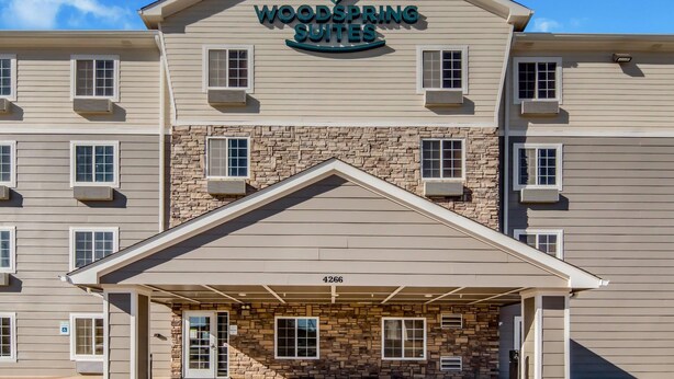 Un hotel de varios pisos con fachada de piedra, cielo despejado y un letrero que dice 'Woodspring Suites'.