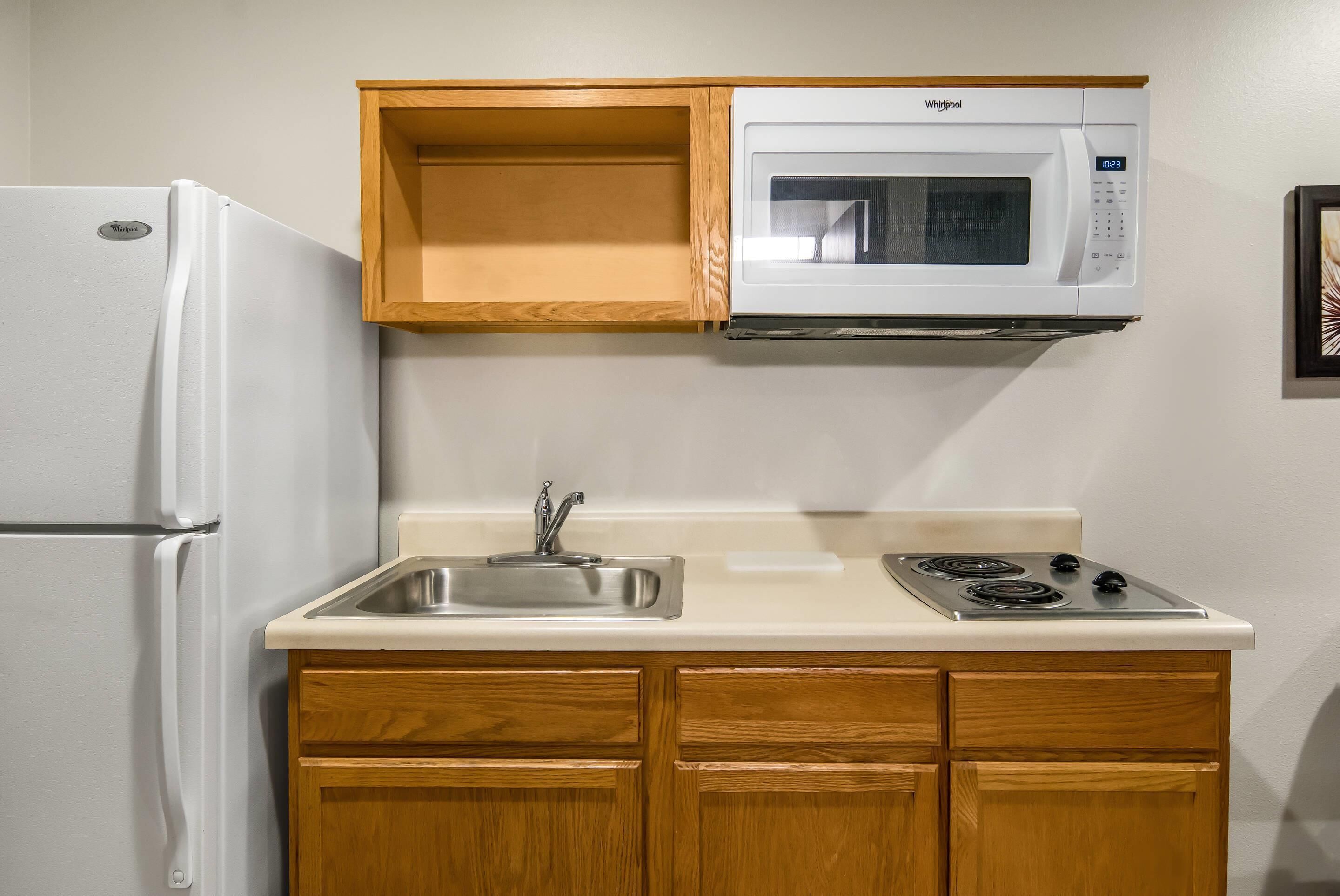 Una cocina compacta con refrigerador, microondas, pileta y muebles de madera.
