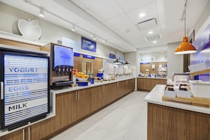 Un área de desayuno moderna con un refrigerador que exhibe yogur, huevos y leche, una estación de cereales y una variedad de frutas y bebidas.
