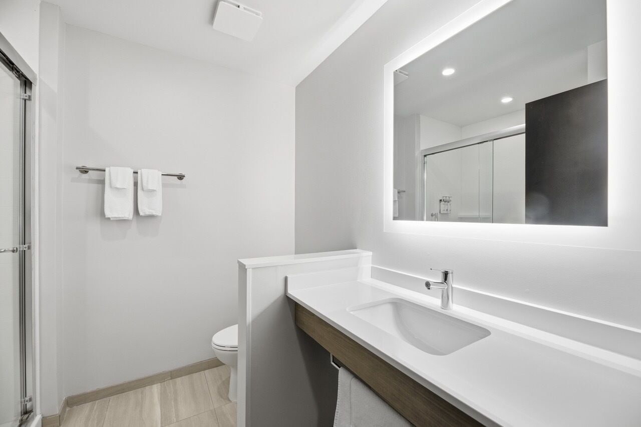 Un baño moderno con un lavabo blanco, un espejo y un perchero para toallas.