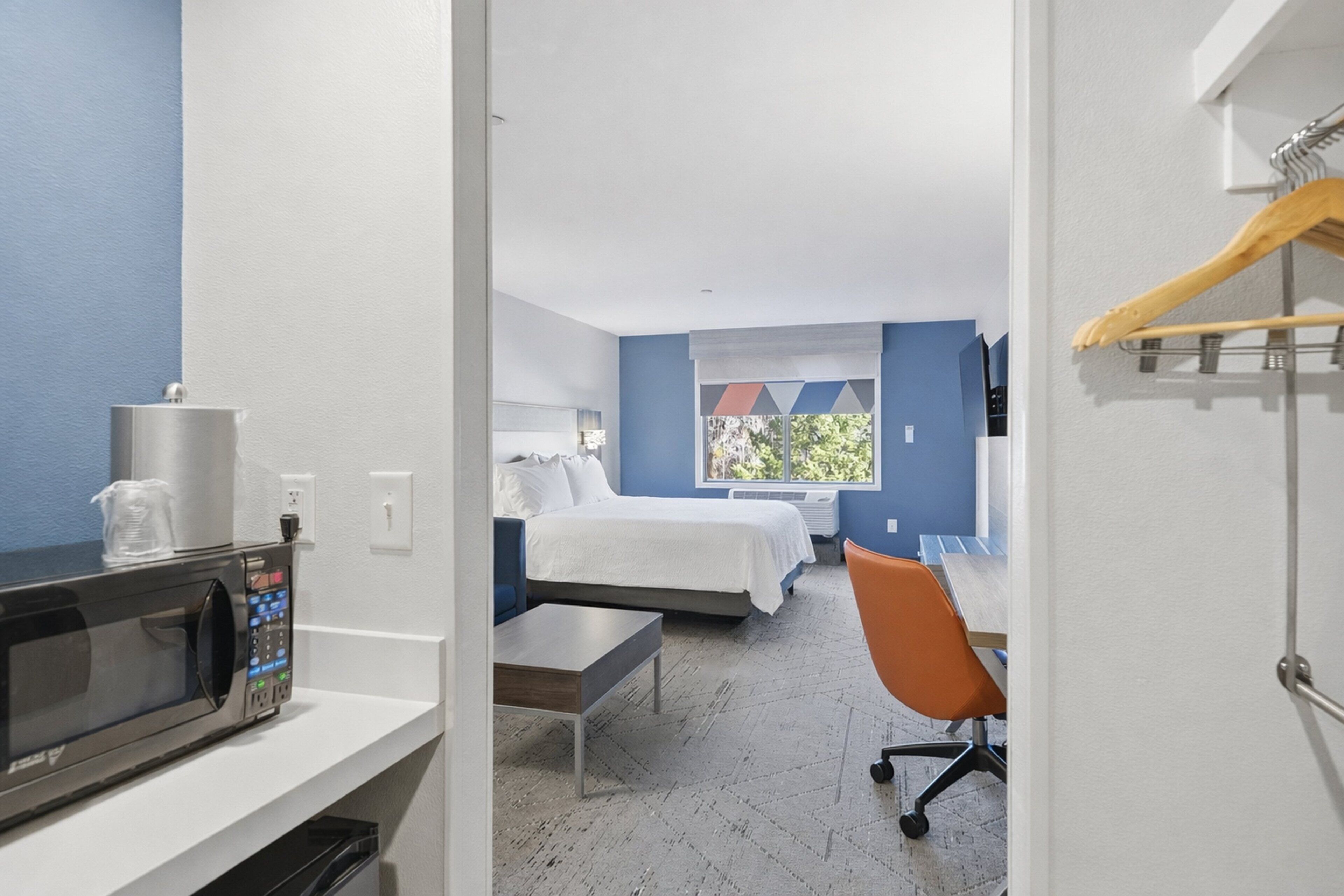 Une chambre d’hôtel équipée d’un lit, d’un bureau, d’une chaise, d’un micro-ondes et d’une fenêtre avec des stores.