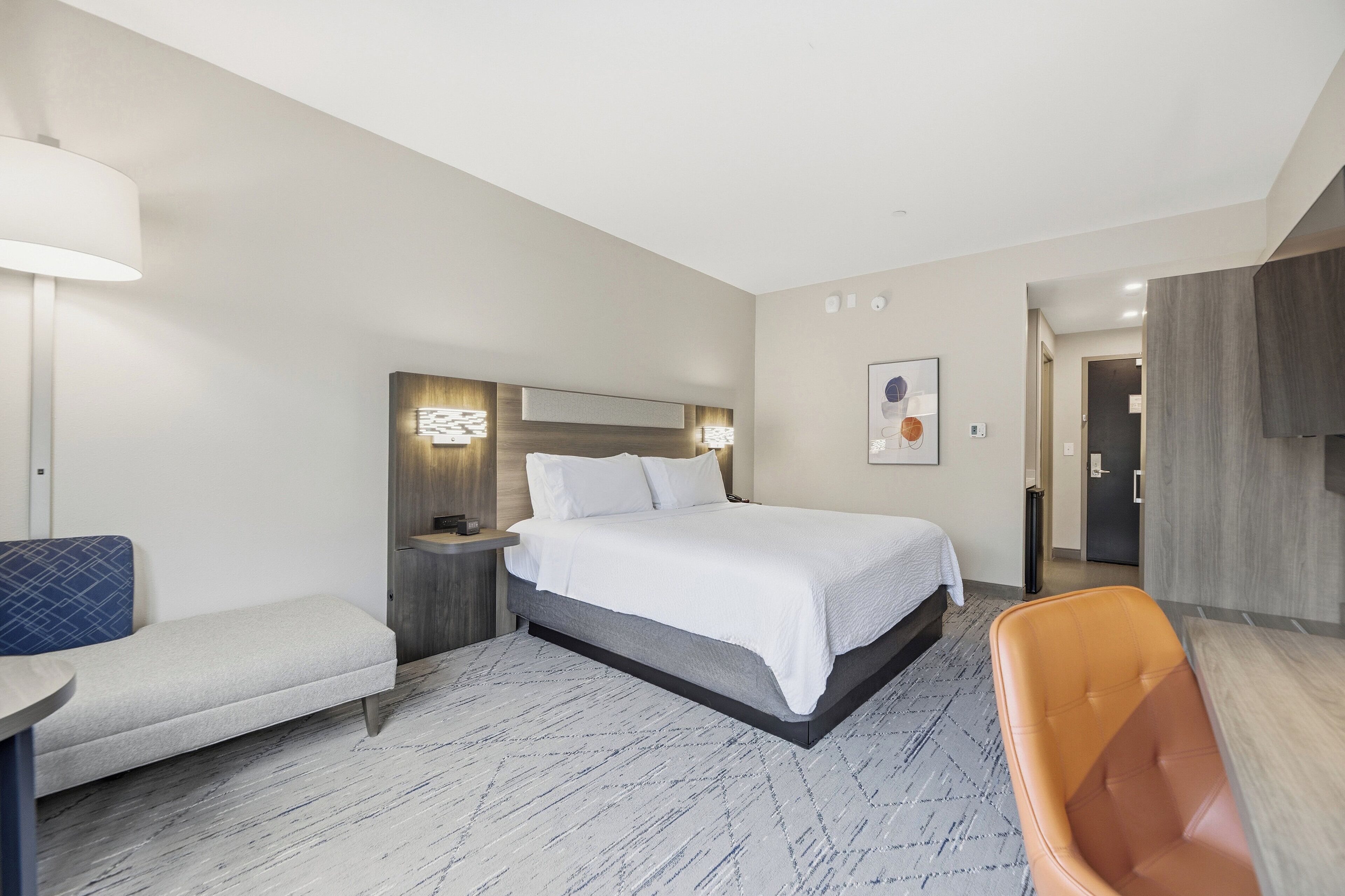 Een moderne hotelkamer met een bed, een bankje, een stoel en een bureau.
