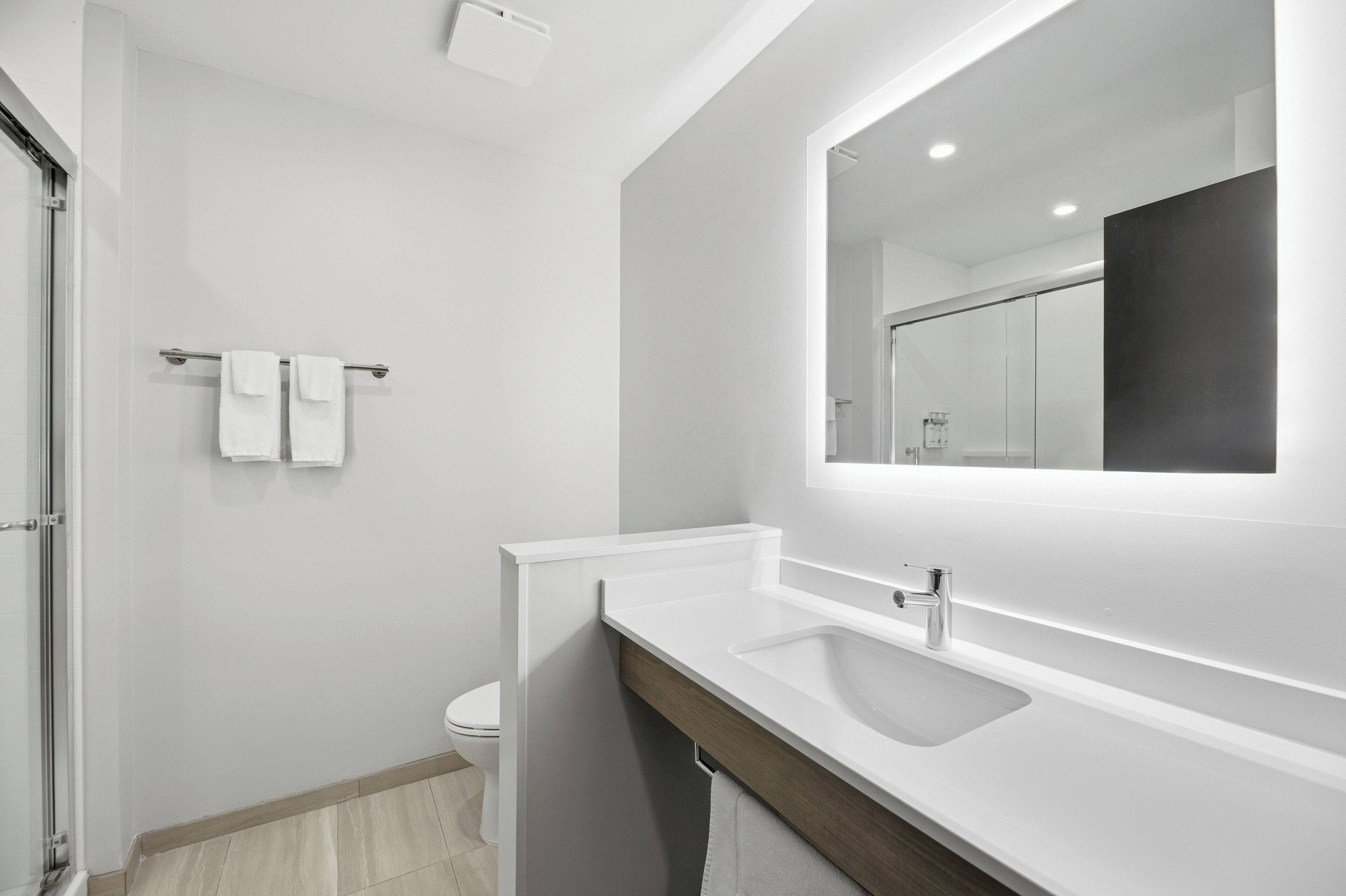 A modern bathroom with a large mirror, white sink, and a towel rack.