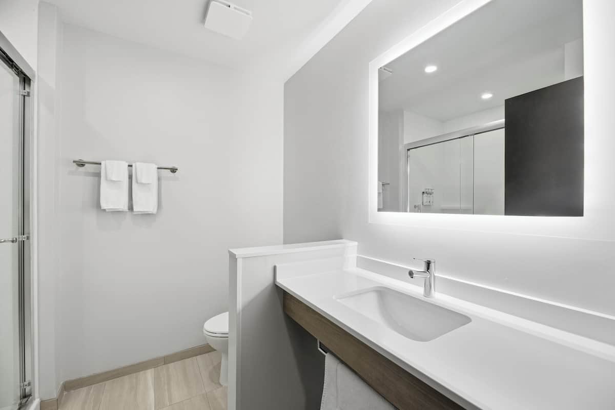A modern bathroom with a large mirror, white sink, and a towel rack.