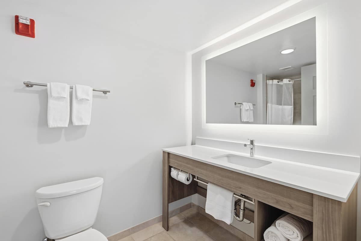 A modern bathroom with a white toilet, a wooden vanity with a sink, a large mirror, and a towel rack with two towels.