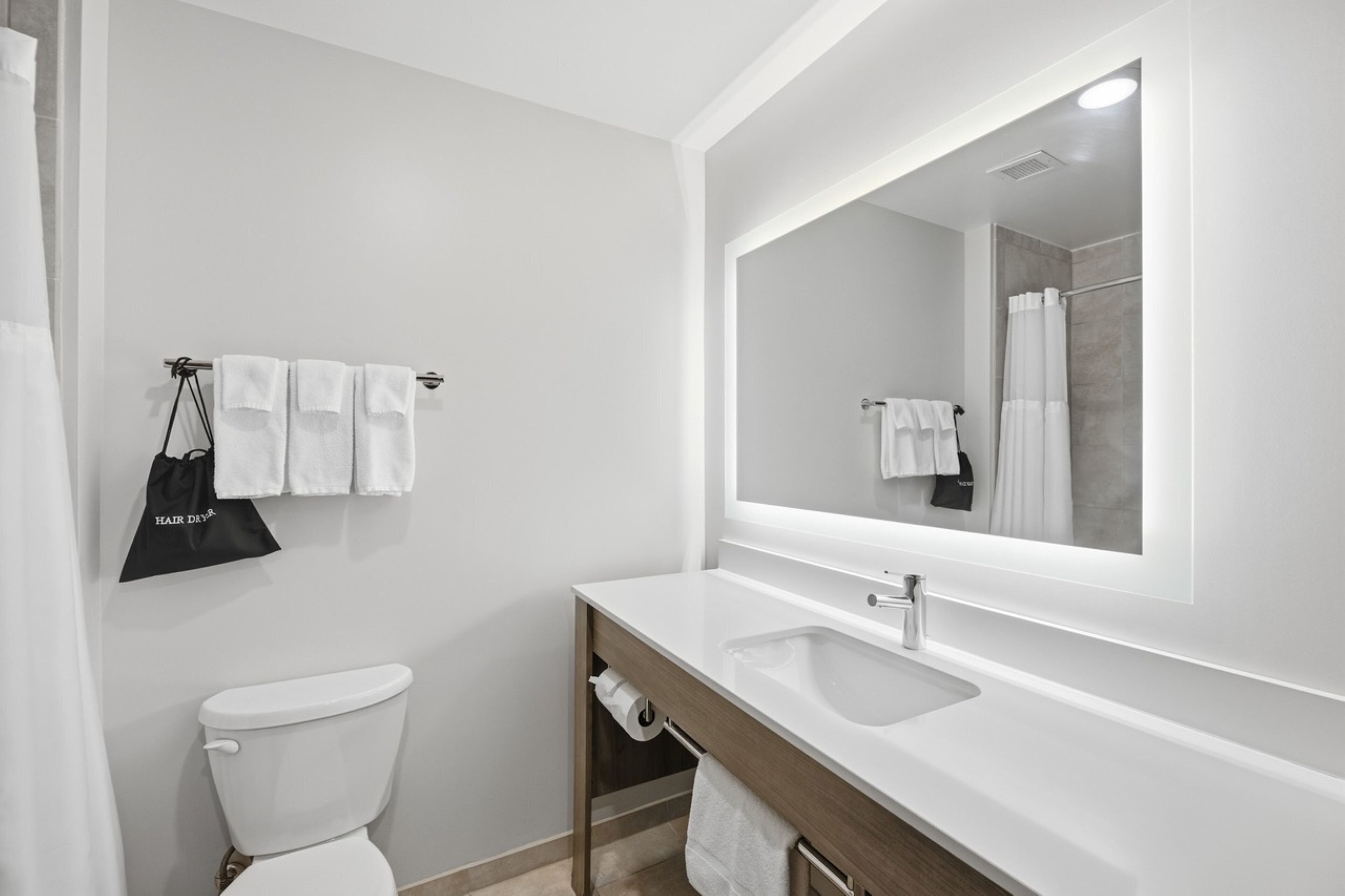 Une salle de bain moderne avec un lavabo blanc, un miroir, des toilettes et un porte-serviettes.