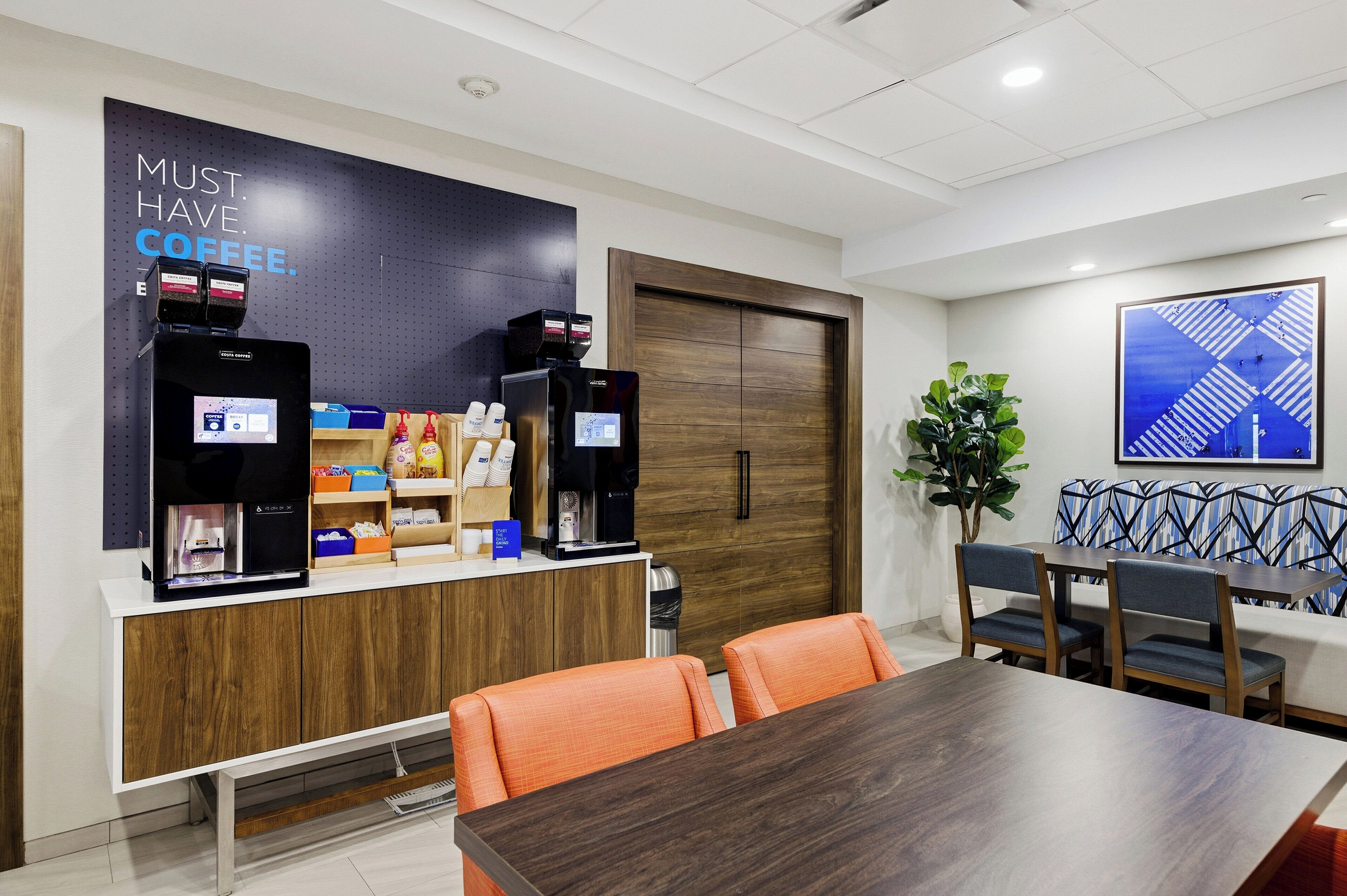 A modern office space with a coffee station, wooden cabinets, and a dining area with orange chairs.