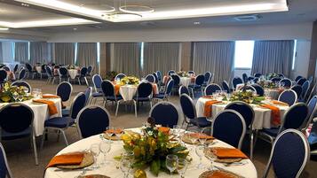 A banquet hall with round tables, blue chairs, and orange napkins.