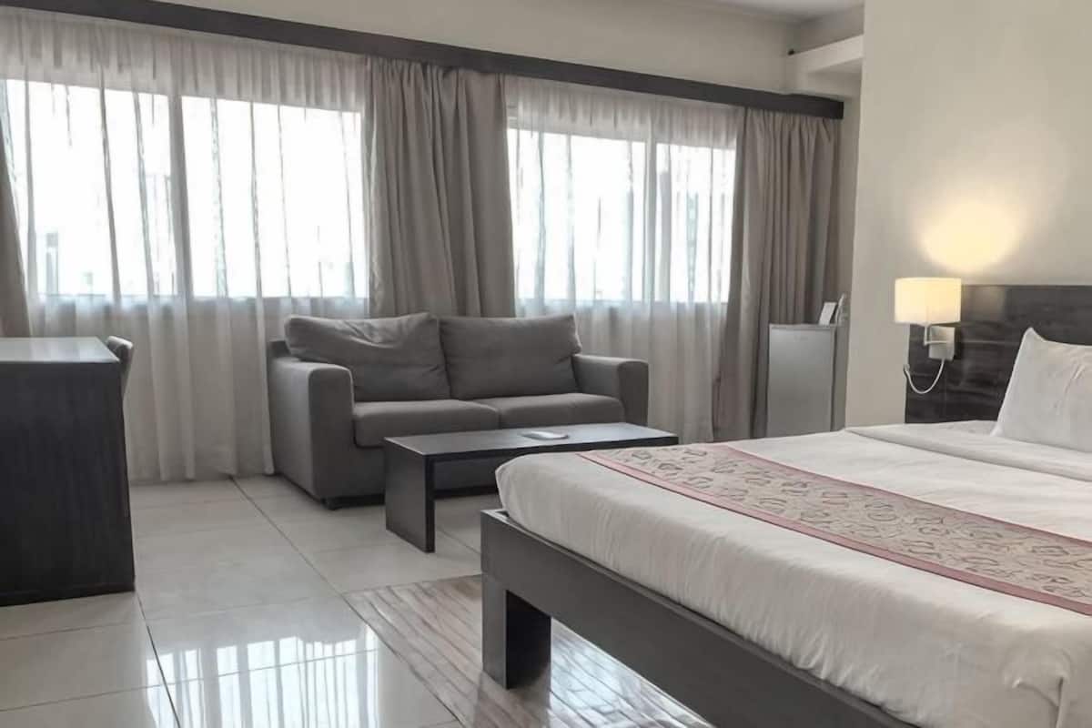 A hotel room with a bed, a sofa, a coffee table, a desk, and a lamp.