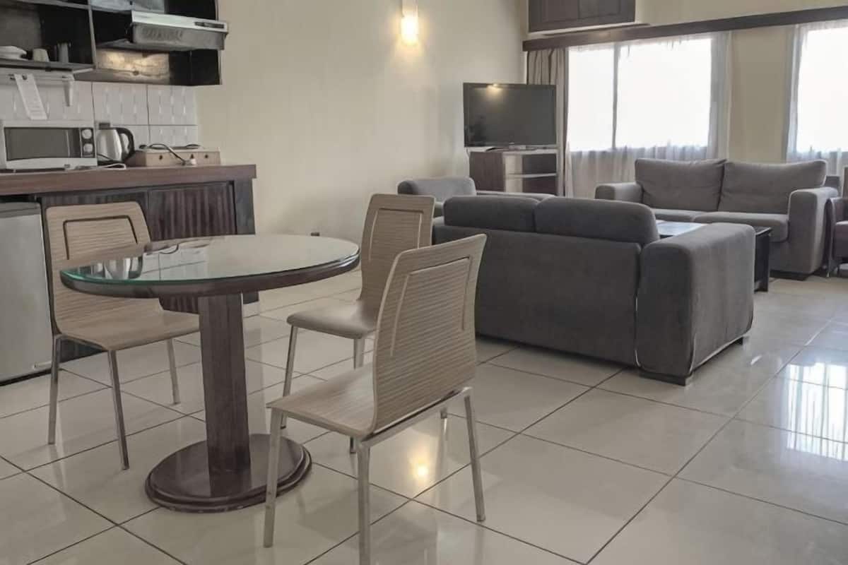 A modern living room with a dining table, grey sofa, and a kitchen area with appliances.