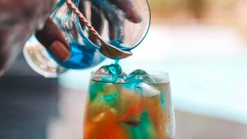 A hand pouring a colorful drink into a glass.