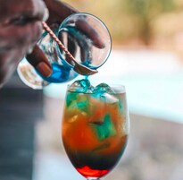 A hand pouring a colorful drink into a glass.