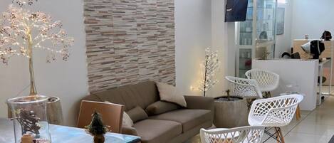 Una sala de estar moderna con sofá, mesa de comedor y sillas. Hay un árbol decorativo y un florero de vidrio sobre la mesa.