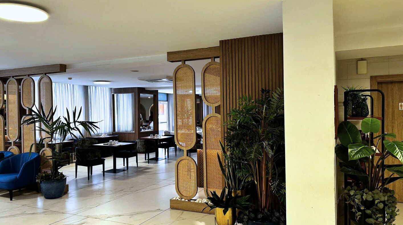 A hotel lobby with a reception desk, seating area, and decorative plants.
