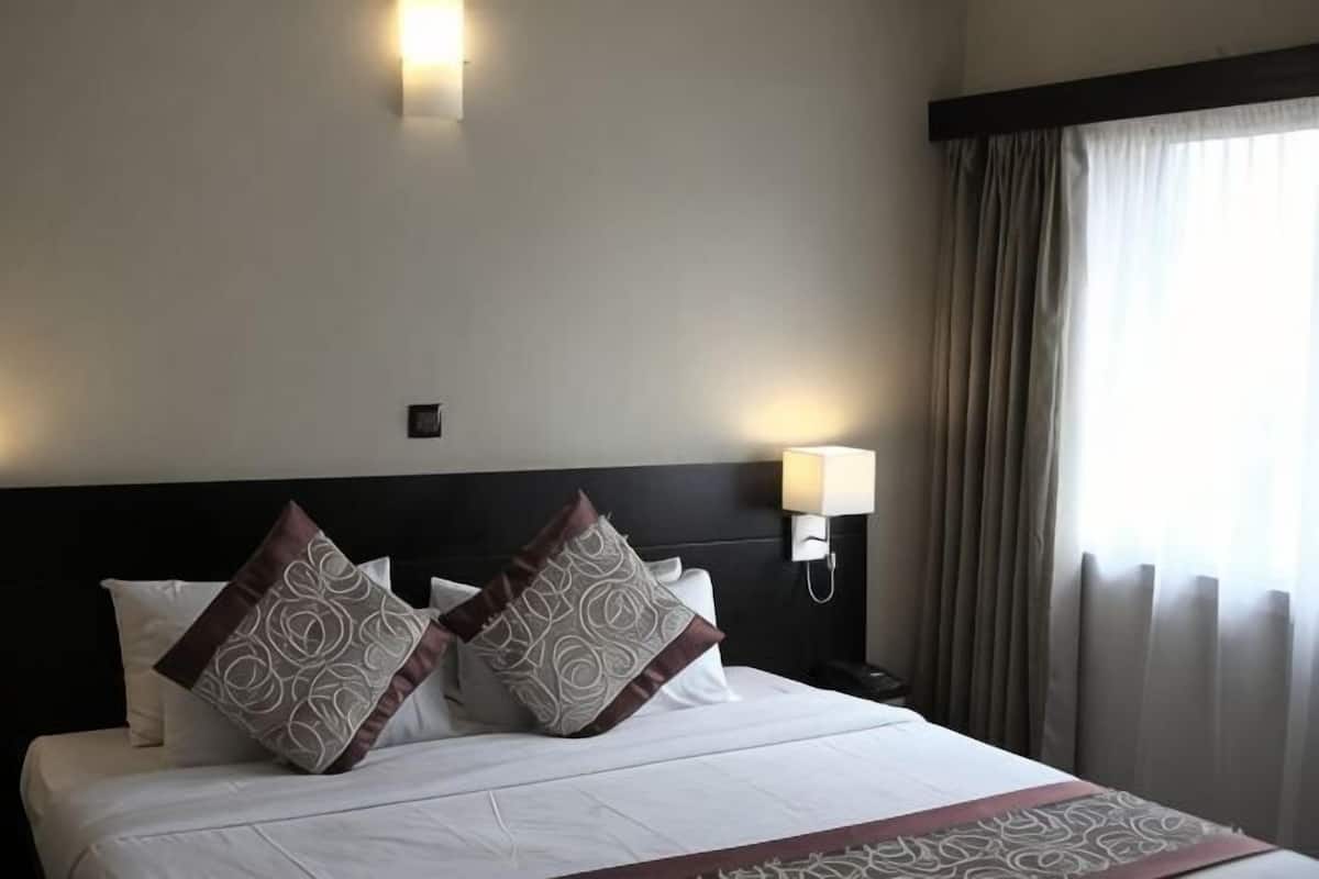 A hotel room with a bed, two wall-mounted lamps, and a window with curtains.