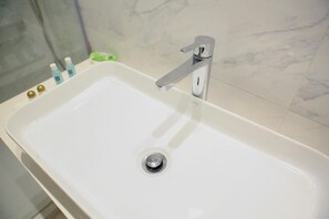 A bathroom with a white sink, a chrome faucet, and a marble backsplash. - Ivotel Abidjan (Abidjan)