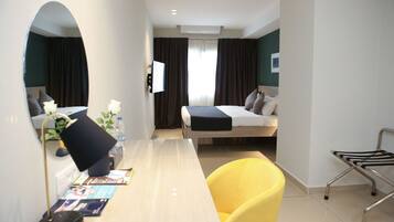 A hotel room with a bed, a desk with a chair, a mirror, and a TV.